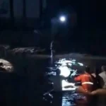 Ilustrasi permukiman tergenang banjir di tepi sungai dengan tanggul karung pasir yang terkikis arus