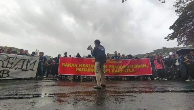 Ilustrasi unjuk rasa di depan Balai Kota Malang saat hujan dengan layar videotron besar di latar