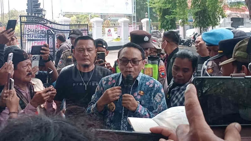 Ilustrasi pendapa kantor bupati dengan bingkai foto kosong di dinding dan spanduk aksi di halaman