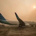 Pesawat di landasan bandara yang diselimuti kabut asap tebal dengan hutan tropis di latar belakang