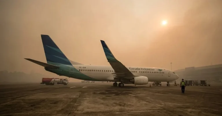 Pesawat di landasan bandara yang diselimuti kabut asap tebal dengan hutan tropis di latar belakang